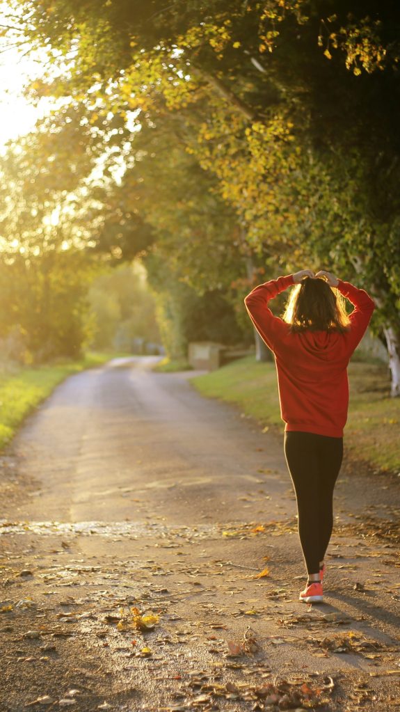 A woman walking down a country road in low angled sunlight.